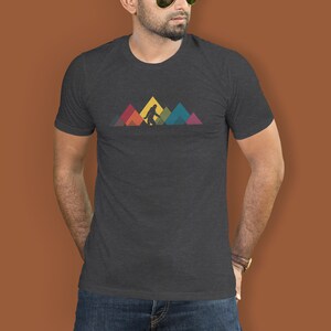 May include: A dark heather grey t-shirt featuring a graphic of Bigfoot walking in front of a rainbow mountain range.