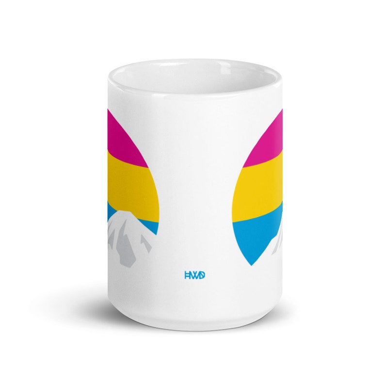 May include: White ceramic mug with a pansexual pride flag design. The flag is in the shape of two half circles with a mountain peak in the center of each. The mug has the text "HWD" on the bottom.