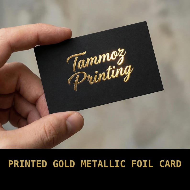 Puede incluir: Una tarjeta de visita rectangular negra con el texto Tammoz Printing en una fuente de escritura de l&aacute;mina de oro met&aacute;lico. La tarjeta tiene un acabado mate y las letras doradas est&aacute;n en relieve, creando una superficie reflectante.