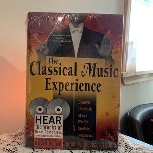 May include: A yellow and gold book titled "The Classical Music Experience" with a conductor on the cover. The book includes two CDs with the text "Hear the Works of Great Composers from Bach to Bernstein" and the names "Kevin Kline" and "Julius H. Jacobson II, M.D."
