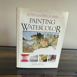May include: A hardcover book titled "Painting in Watercolor" from The Artist's Handbook Series. The cover features a watercolor painting of a landscape with a building and trees. The book includes sections on techniques, materials, demonstrations, and finishing.