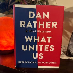 May include: A hardcover book titled "What Unites Us" by Dan Rather and Elliot Kirschner. The book's cover is split vertically, with a blue section on the left and a red section on the right. White text is used for the title and author names.