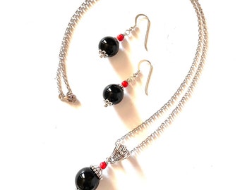 May include: A silver chain necklace and earrings set with black beads and red accents.