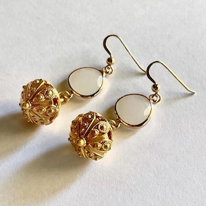 Könnte beinhalten: Goldfarbene Ohrhänger mit weißen runden Steinen und einem detaillierten Kugeldesign.