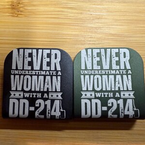 May include: Two black and green coasters with white text that reads "Never underestimate a woman with a DD-214".