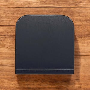 May include: A dark blue, rectangular napkin holder made of wood. The holder has a rounded top and bottom.