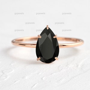 Könnte beinhalten: Ein Ring aus Roségold mit einem birnenförmigen schwarzen Onyx-Edelstein. Der Ring ist schlicht und elegant mit einem zarten Band.