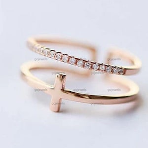 以下が含まれることがあります： 繊細な十字架のデザインと輝くキュービックジルコニアのバンドが施された、ローズゴールドのリングです。