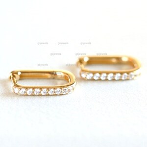 May include: A pair of gold square hoop earrings with a row of clear cubic zirconia stones around the edge.