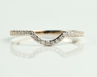 May include: A delicate, curved gold ring, encrusted with small, sparkling diamonds. The ring's design features a gentle arch, with the diamonds set along the top and front surfaces. The ring is displayed on a reflective surface.