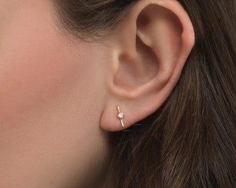 May include: A close-up of a person's ear with a small gold earring featuring a single diamond.