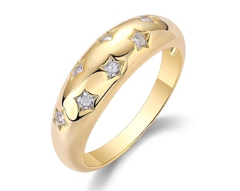 May include: A gold-colored ring with a domed surface, featuring embedded star-shaped designs. Each star is adorned with a small, clear gemstone. The ring has a polished finish, reflecting light. A piece of jewelry.