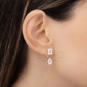 May include: Gold earrings with a square-shaped clear stone and a dangling pear-shaped clear stone.
