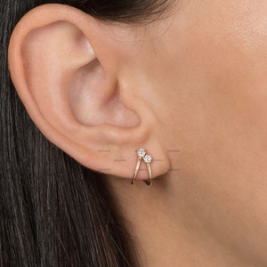 May include: Gold hoop earrings with two small clear cubic zirconia stones. The earrings are designed to be worn in the upper ear cartilage.