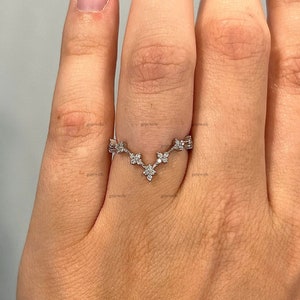 May include: A delicate silver ring with a V-shaped design featuring small, sparkling diamonds. The ring is worn on a finger.