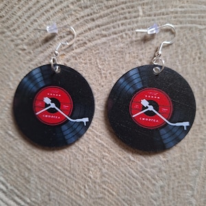 May include: A pair of black vinyl record earrings with red labels and white turntable arm details. The earrings have silver-colored fish hook ear wires. The earrings are round and have a retro music theme.