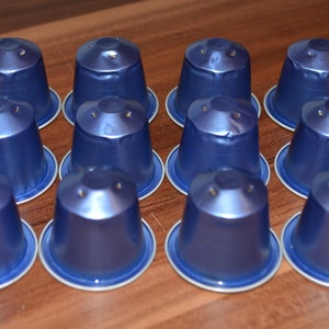 Puede incluir: Doce cápsulas de café azules dispuestas en forma triangular sobre una superficie de madera.