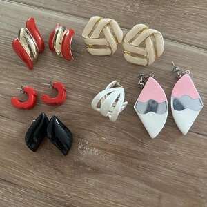 Könnte beinhalten: Eine Sammlung von Vintage-Ohrringen in verschiedenen Stilen und Farben. Enthält rote, goldene, schwarze, weiße und rosa Ohrringe. Zu den Stilen gehören Creolen, geometrische Formen und abstrakte Designs.