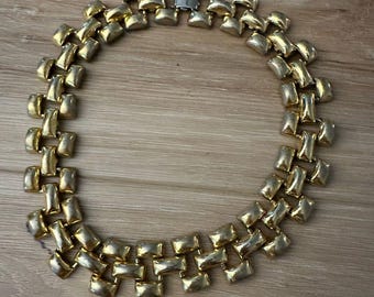 May include: A gold tone chain necklace with a linked design. The links are rectangular and interlock with each other.