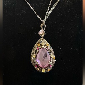 May include: A silver chain necklace with a teardrop-shaped pendant. The pendant is adorned with a large pink rhinestone surrounded by smaller rhinestones in various colors, including yellow, orange, pink, and blue.