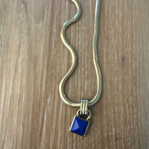 May include: A gold chain necklace with a square pendant featuring a blue gemstone.