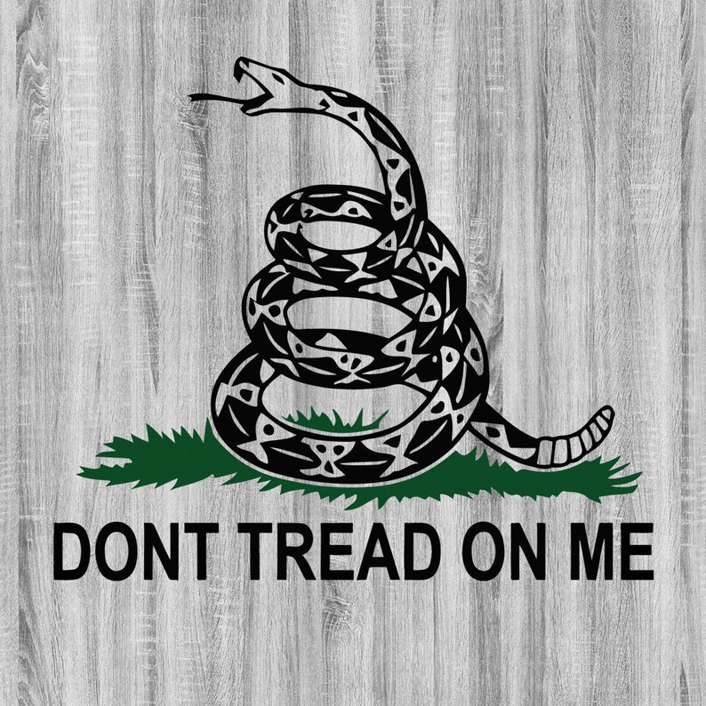 Op de afbeelding: Een zwart-wit illustratie van een opgerolde slang met uitgestoken tong, op groen gras. De woorden "DONT TREAD ON ME" zijn eronder in zwart gedrukt, tegen een lichtgrijze houtnerf achtergrond.