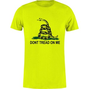 Op de afbeelding: Een felgeel t-shirt met een opgerolde ratelslang in zwart en geel, boven de zwarte tekst "DONT TREAD ON ME". Het shirt heeft een ronde hals.