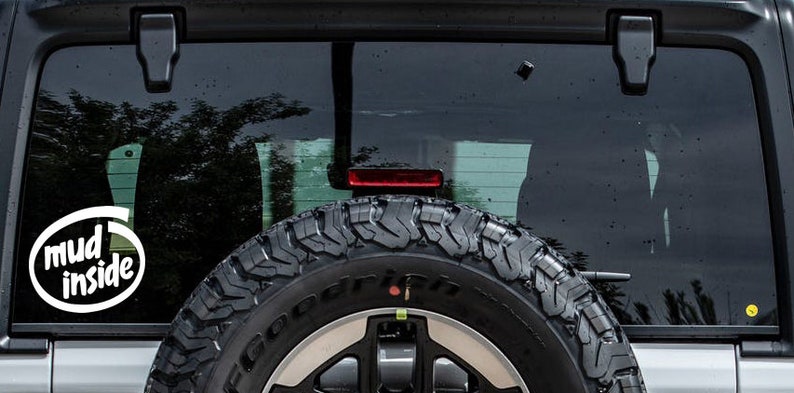 May include: A white vinyl sticker on the back window of a silver car. The sticker says "mud inside" in a white oval with a black outline.