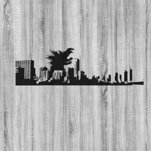 Op de afbeelding: Zwart silhouet van een skyline met een Godzilla-figuur die boven de gebouwen uittorent. Het ontwerp is geplaatst tegen een lichtgrijze houtnerf achtergrond, wat een opvallend contrast creëert.