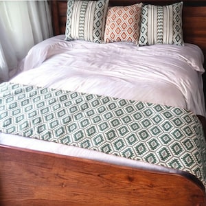 Può includere: Un letto bianco con un copriletto a motivi verdi e bianchi. Il letto ha una testiera e un piede in legno. Ci sono tre cuscini sul letto, due con un motivo geometrico bianco e verde e uno con un motivo geometrico rosso e arancione.
