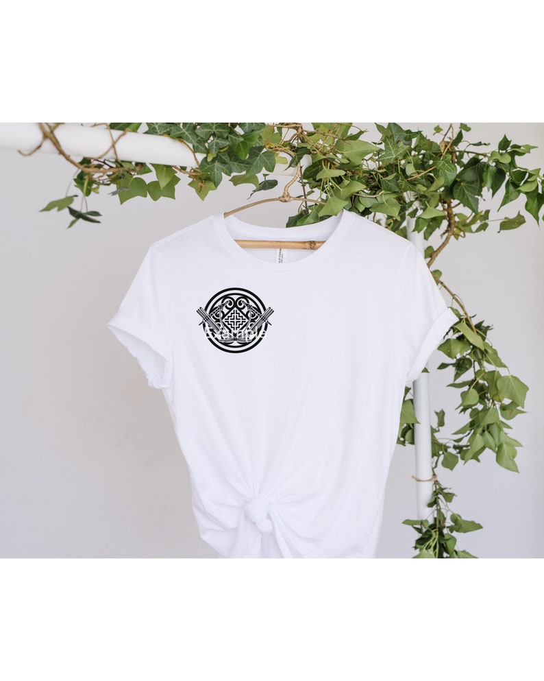 May include: White t-shirt with a black and white graphic design of a circular pattern with two swords crossing in the center.