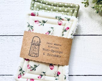 May include: Three reusable kitchen scrubbers with floral patterns. The top scrubber is green with white polka dots. The middle scrubber is cream with pink roses. The bottom scrubber is white with a pink rose pattern. The scrubbers are packaged with a brown paper label that reads "Zero Waste Kitchen Non-Sponge & Scrubby" and a logo for "The Eco Cottage".