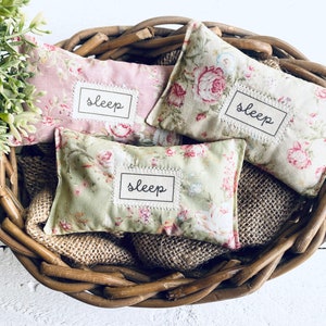 May include: Three floral fabric sleep pillows in a wicker basket. Each pillow has a white label with the word "sleep" written in black.