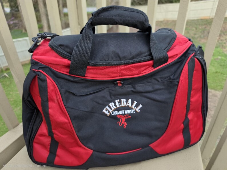 K&ouml;nnte beinhalten: Eine schwarz-rote Reisetasche mit oberem Griff und Schultergurt. Auf der Tasche steht in Wei&szlig; der Schriftzug "Fireball Cinnamon Whisky" mit einem roten Logo. Die Tasche liegt auf einer Holzoberfl&auml;che.
