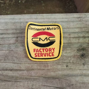 May include: Yellow fabric patch with black and red embroidery. The patch reads "Continental Motors" and "CMC" in a circle with a red stripe. Below the circle is the text "Factory Service".