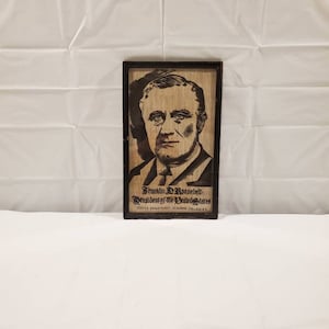 Könnte beinhalten: Ein gerahmtes Schwarzweißporträt von Franklin D. Roosevelt, Präsident der Vereinigten Staaten. Der Rahmen ist aus Holz und hat eine dunkelbraune Oberfläche. Der Text "Franklin D. Roosevelt - Präsident der Vereinigten Staaten" ist unter dem Porträt gedruckt. Der Text "Textile Department, Clemson College, S.C." ist unter dem Text gedruckt.
