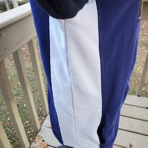 May include: A blue and white hooded sweatshirt with a white vertical stripe down the side. The sweatshirt has a black hood and a zippered pocket. The garment is displayed on a mannequin.