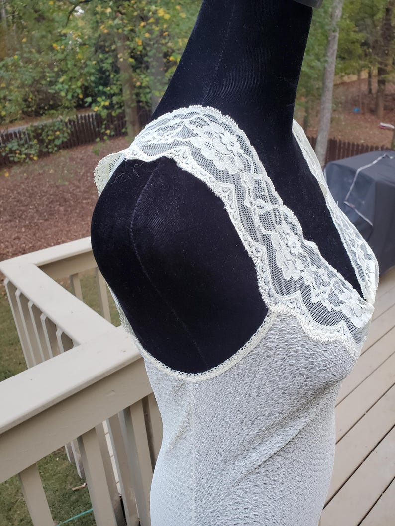 Puede incluir: Un vestido de slip blanco con ribete de encaje y una tela transparente y texturizada.