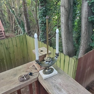 Peut inclure: Une lampe de table dorée avec deux ampoules en forme de bougie. La lampe a une base décorative et repose sur une base en marbre blanc.