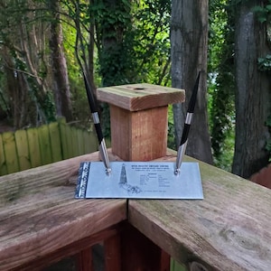 Puede incluir: Un portaplumas de metal plateado con dos bolígrafos negros. El portaplumas presenta un gráfico de un edificio con el texto "New York Madison Square Garden" y una lista de eventos.