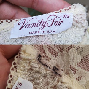 Puede incluir: Una etiqueta de prenda de encaje blanco con el texto "Vanity Fair" en letras marrones y "XS" en letras negras. La etiqueta tambi&eacute;n dice "Made in U.S.A."