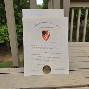 Könnte beinhalten: Eine Abschlussurkunde für Technische Überwachungswissenschaften. Das Dokument hat ein goldenes Siegel und ein rotes, schwarzes und gelbes Emblem. Der Text enthält "Certificate of Graduation" und "16. November 1990".