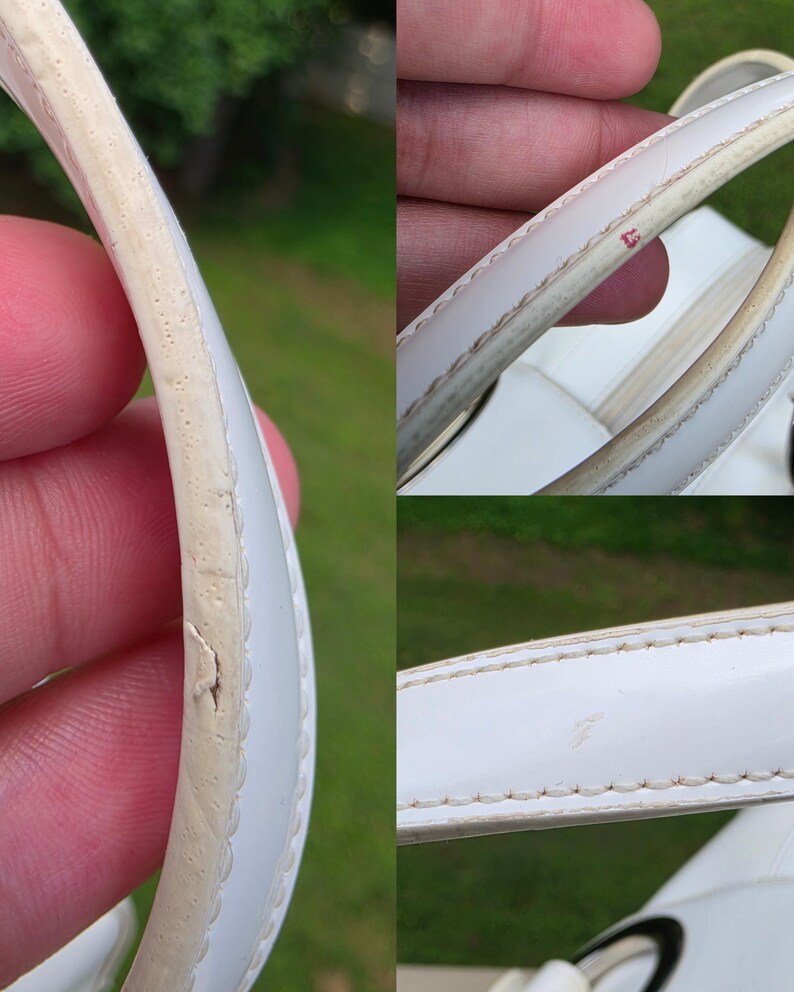 Op de afbeelding: Een wit handtashengsel met zichtbare slijtage langs de randen. Het hengsel vertoont tekenen van barsten, afbladdering en verkleuring op de rand, samen met een kleine rode vlek en lichte krassen op het witte materiaal.