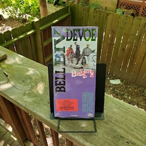 May include: A purple and gold album cover with the title "DeVoe" and the text "Belle Biv DeVoe" on the side. The album cover features three men in black and white clothing standing in front of a car. The text on the album cover reads "Our music is mentally hip hop smoothed out on the R&B tip with a pop feel appeal to it."