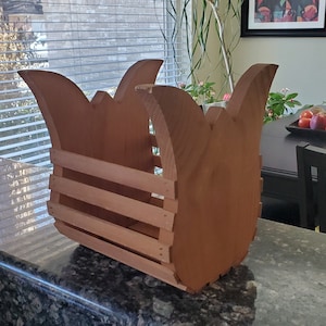 May include: A wooden planter with a unique, curved design. The planter is made of natural wood and has a light brown color. It features a series of horizontal slats for drainage and support.