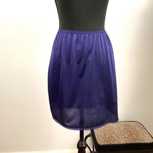 May include: A dark blue slip skirt with a lace trim. The skirt is on a mannequin and is displayed on a wooden floor.