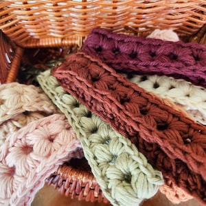 Pode incluir: Uma cesta de vime cheia de tiras de croch&ecirc; em v&aacute;rias cores, incluindo rosa, verde, marrom e bord&ocirc;. As tiras s&atilde;o feitas com um padr&atilde;o de ponto texturizado.