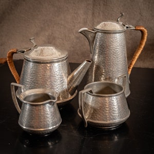 Pode incluir: Um conjunto de quatro bules de chá de metal martelado prateado com alças de couro castanho. Os bules de chá estão dispostos sobre uma superfície preta.
