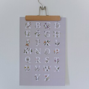 May include: A light purple poster with the alphabet printed in white. Each letter is surrounded by a floral design with different colored flowers.