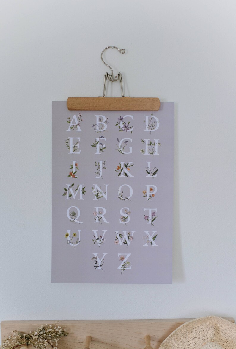 May include: A light purple poster with the alphabet printed in white. Each letter is surrounded by a floral design with different colored flowers.